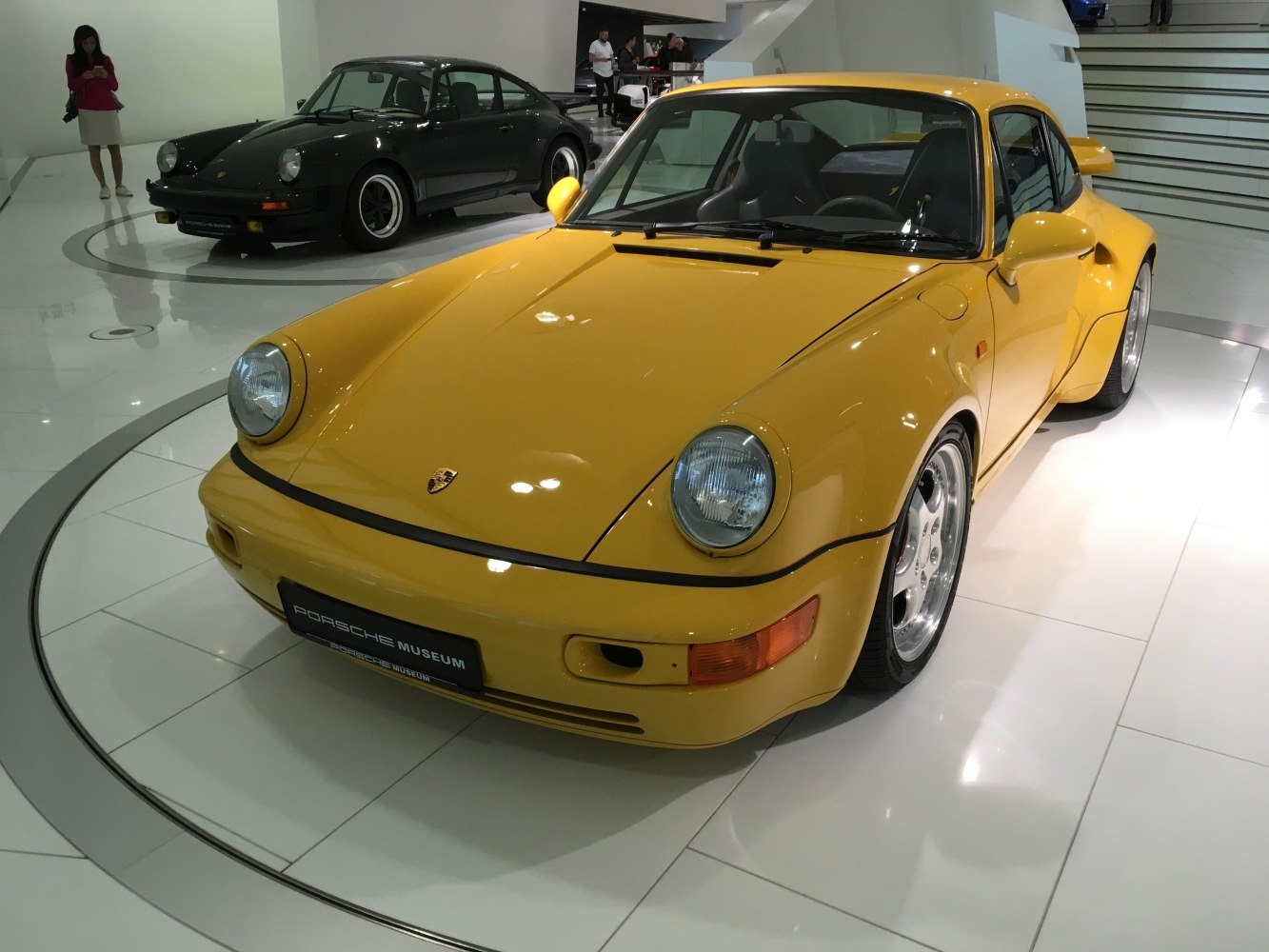 Yellow Porsche 911 964 with widebody fenders, clear headlights from front angle.