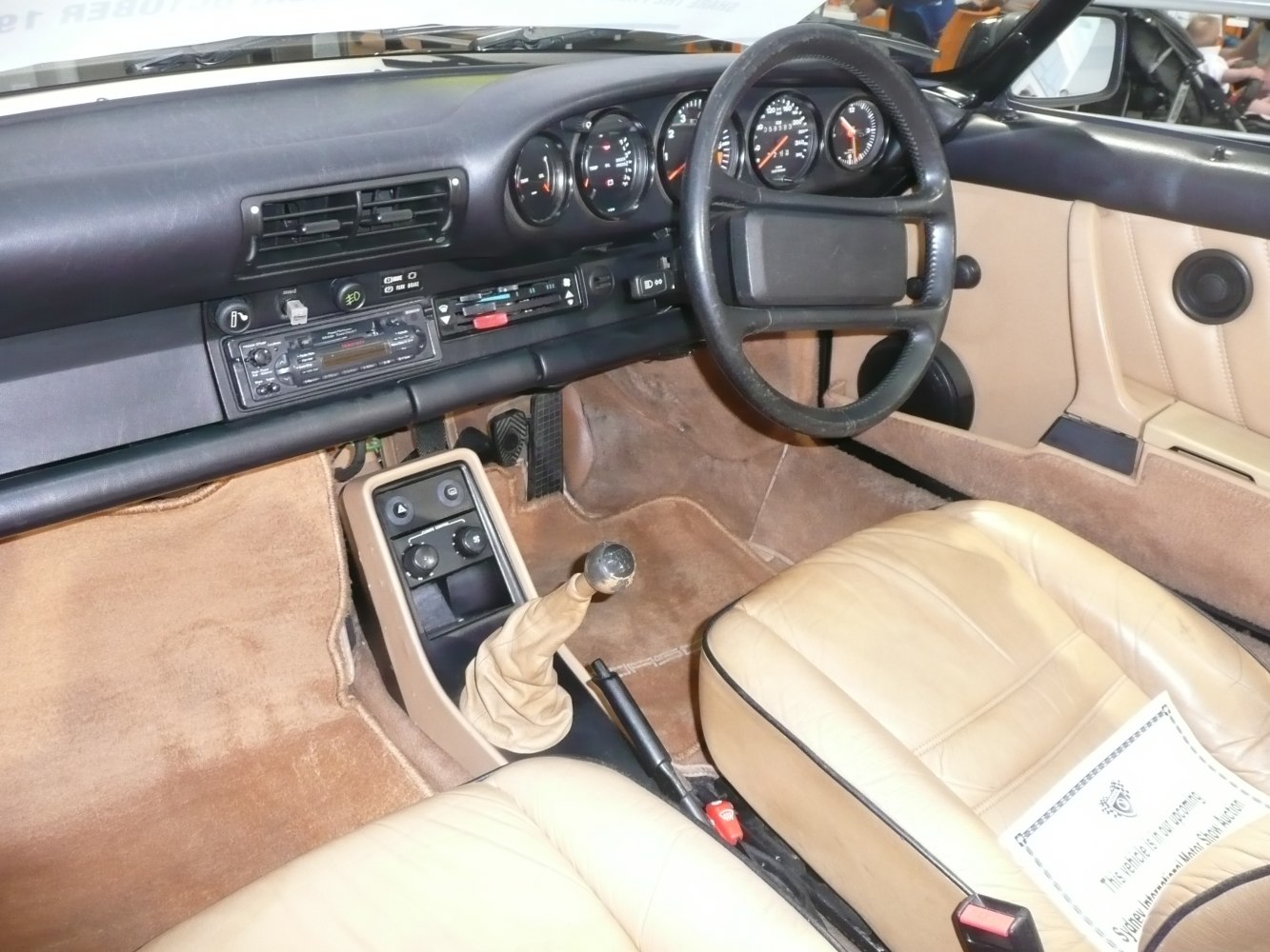 Manual gear shift, analog gauges, tan leather seats in vintage car interior