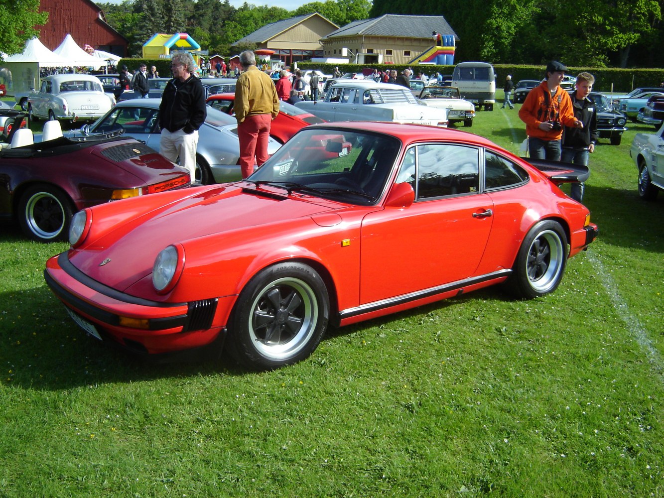 Red coupe with wide fenders and whale tail spoiler on green lawn.