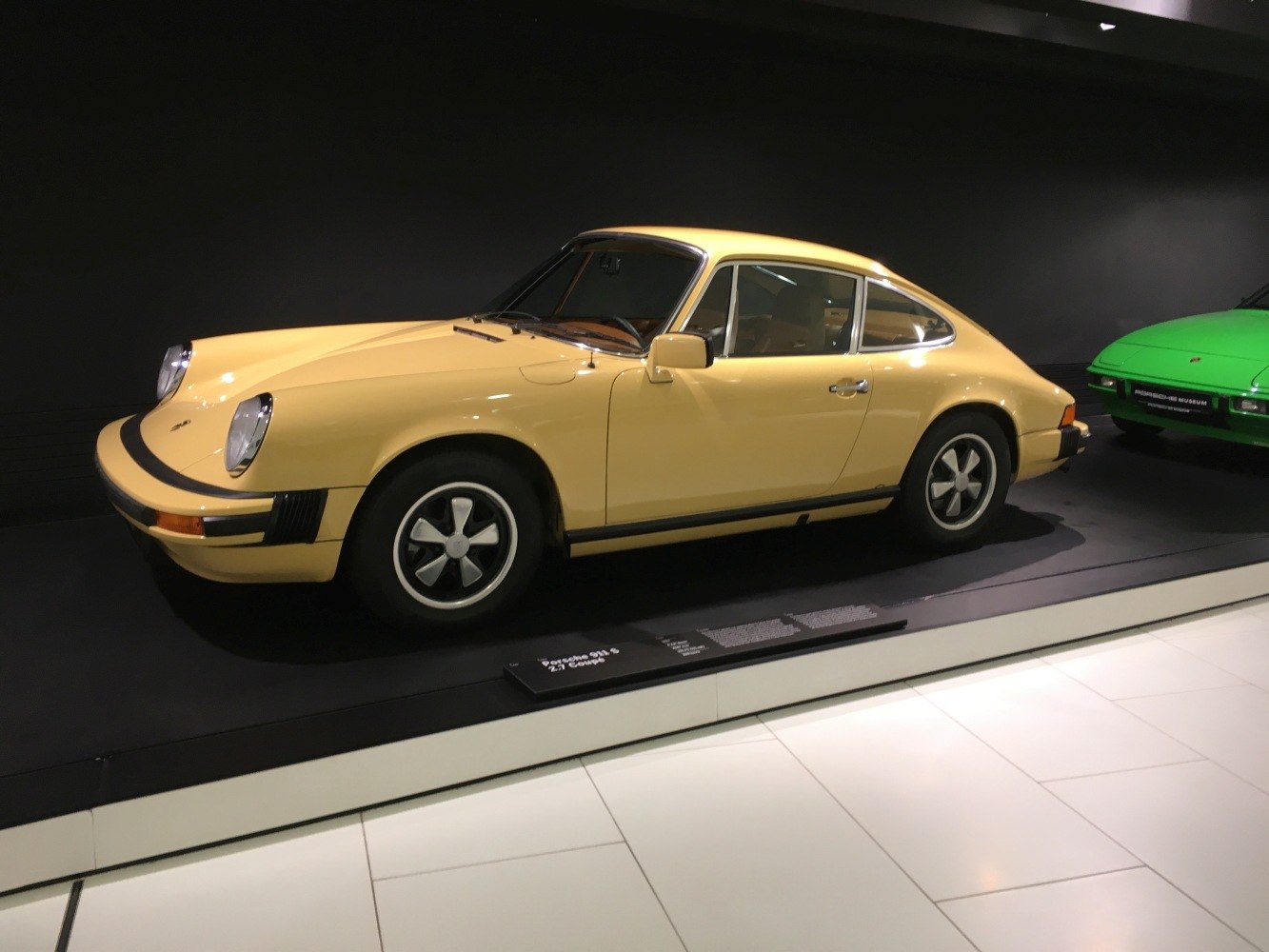 Side profile of a vintage yellow sports coupe with round headlights and classic wheels.