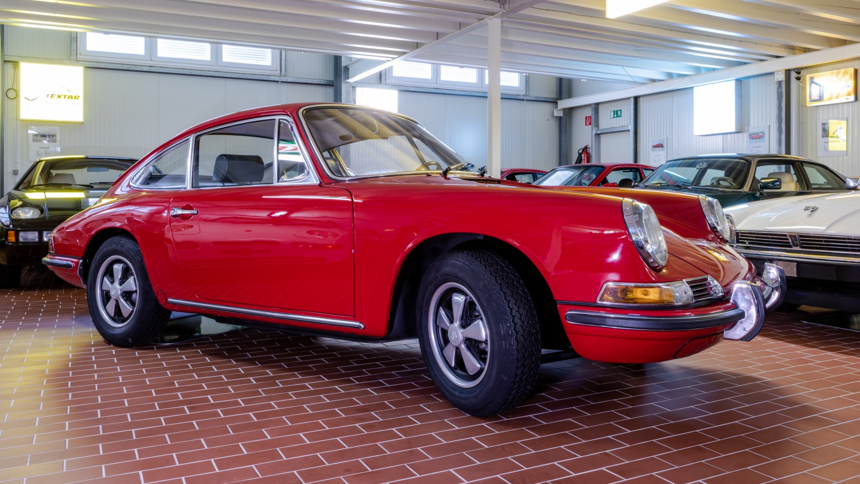 Red vintage coupe with round headlights, chrome bumper guards, classic five-spoke wheels.