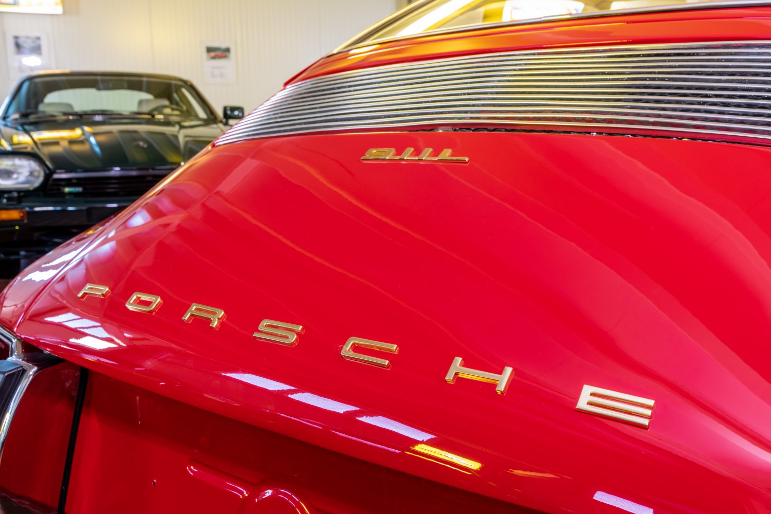 Close-up of rear decklid with metal grill and car emblem in shiny red paint.