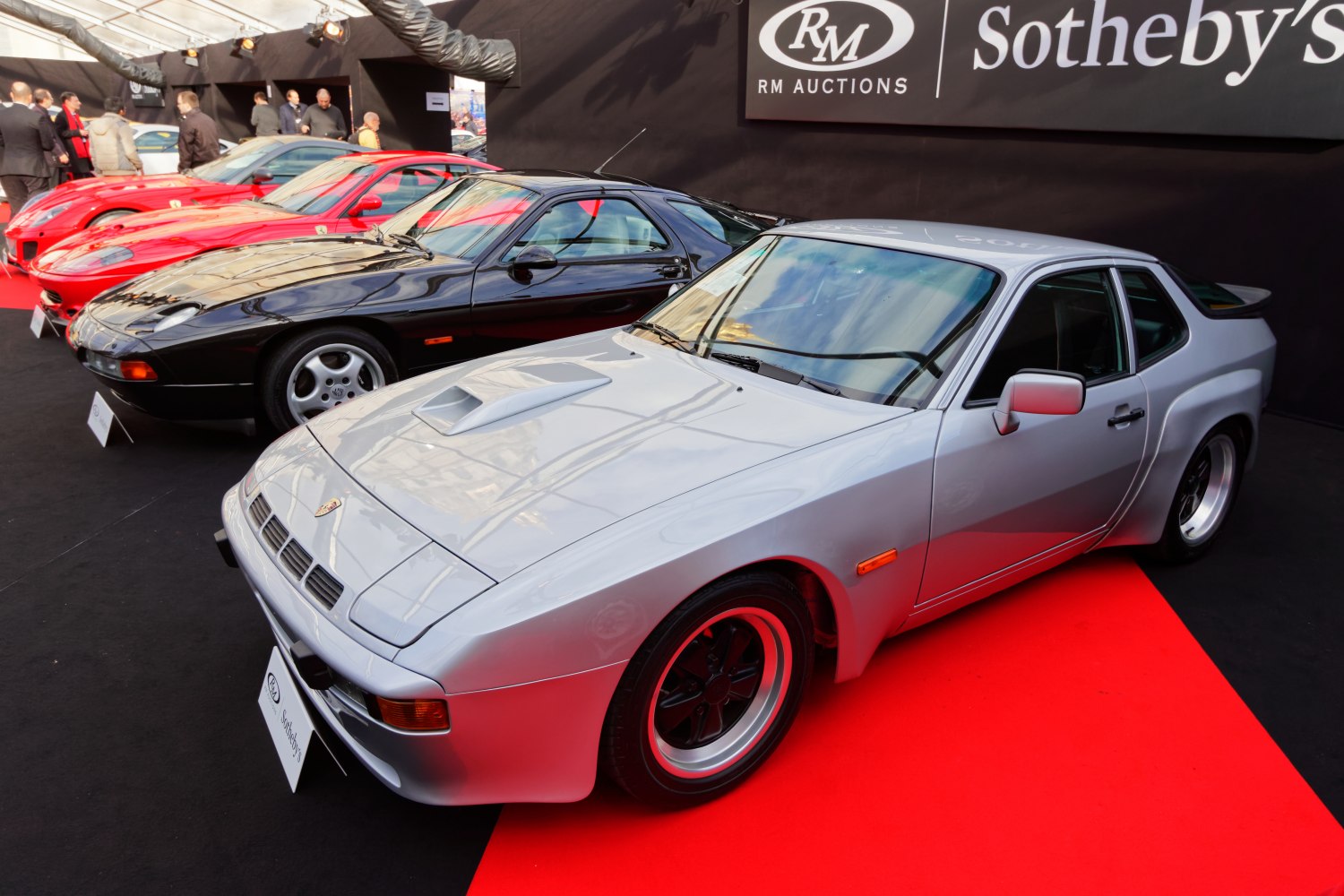 Silver coupe with front hood scoop and distinctive wheel style on red and black floor