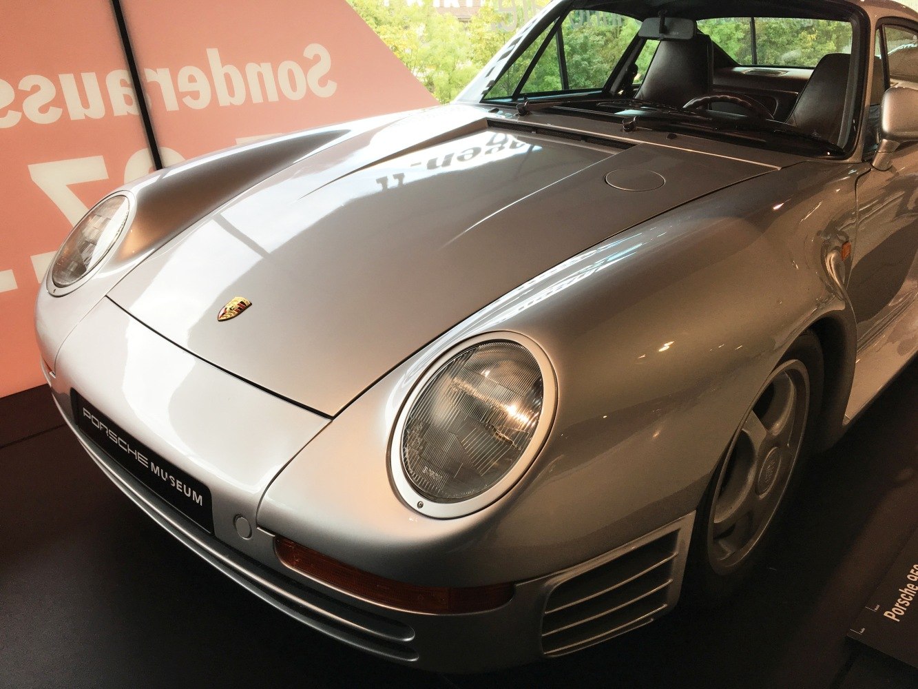 Close-up of a silver sports car front with round headlights and aerodynamic design.