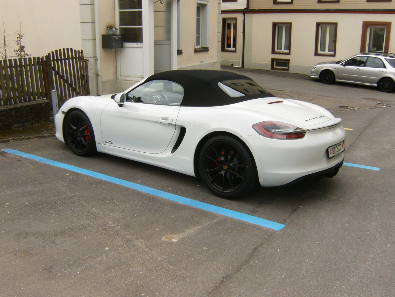 White convertible with black soft top, rear spoiler, and black alloy wheels