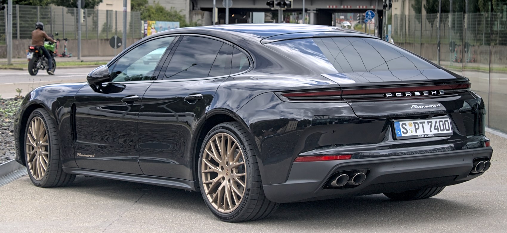 Black luxury sedan rear view with bronze multi-spoke wheels and quad exhaust.