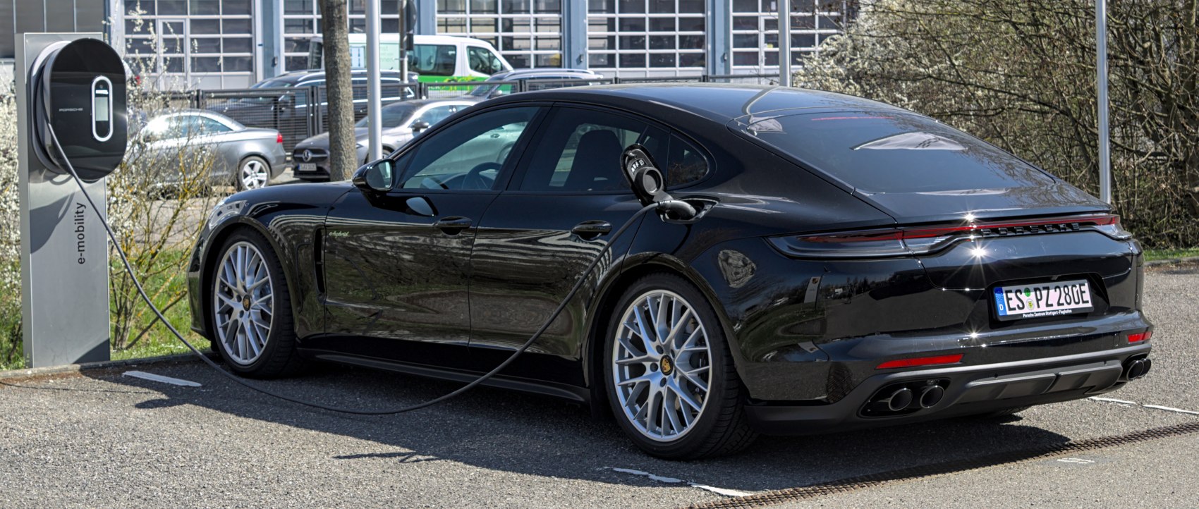 Rear side view of a plug-in hybrid luxury sedan connected to a charging station