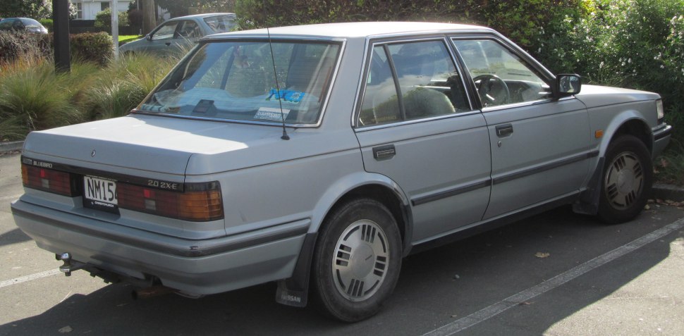 Rear and side view of a classic boxy sedan with vintage wheel covers.