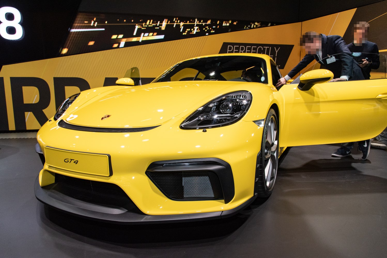Yellow Porsche 718 Cayman GT4 front view with open door and detailed headlights