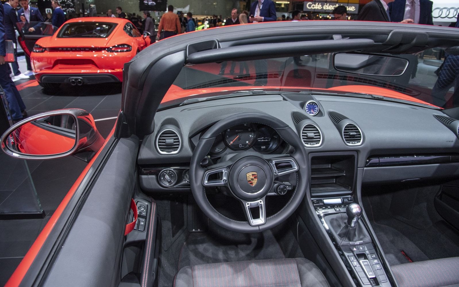 Convertible cockpit with sporty steering wheel and rear view of a red sports car.