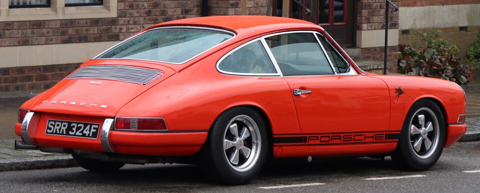Rear-side view of a classic orange sports coupe with Porsche side stripe