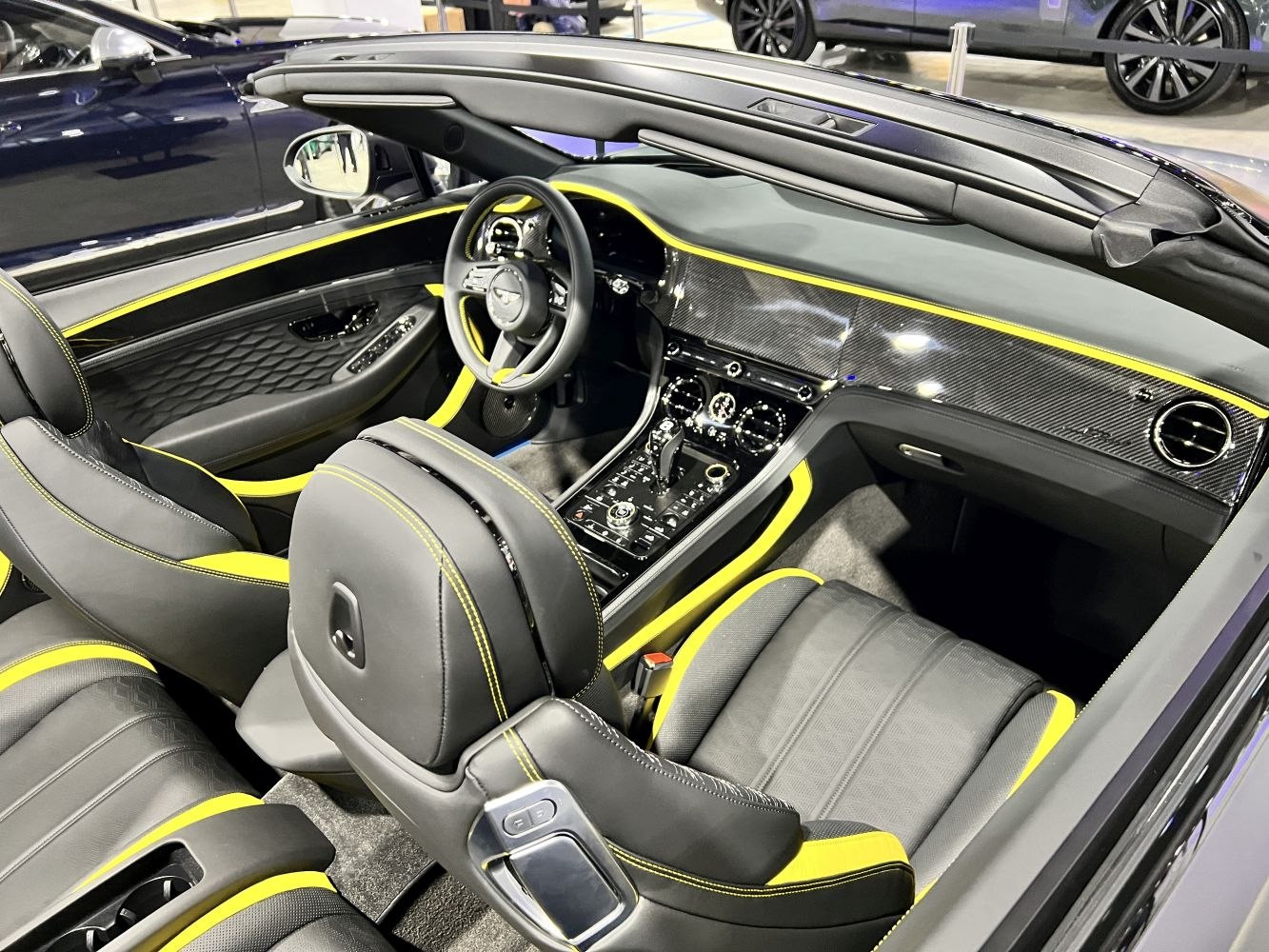 Luxury convertible interior with carbon fiber dashboard and yellow trim accents.