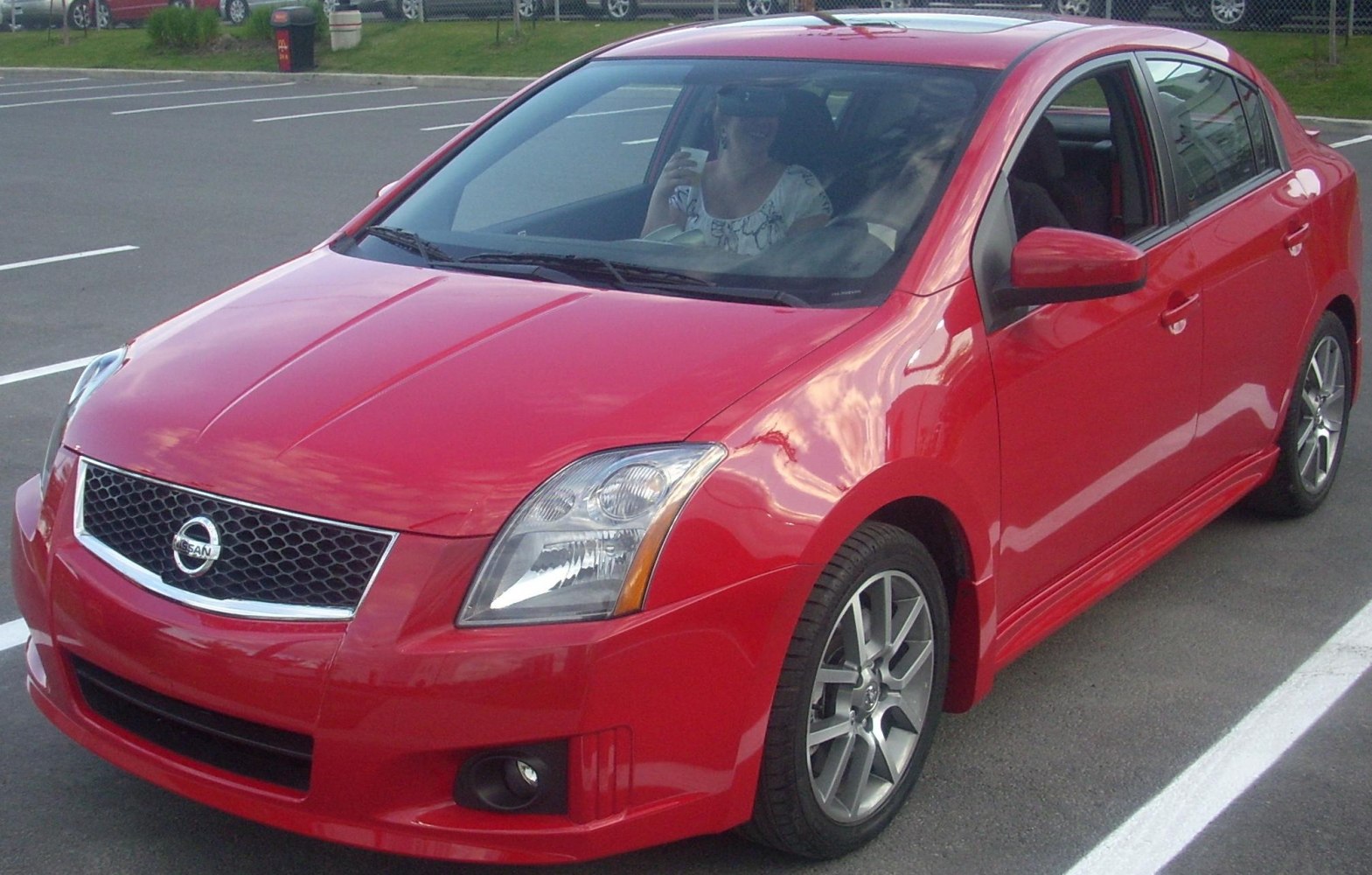 Red sedan with chrome mesh grille and alloy wheels.