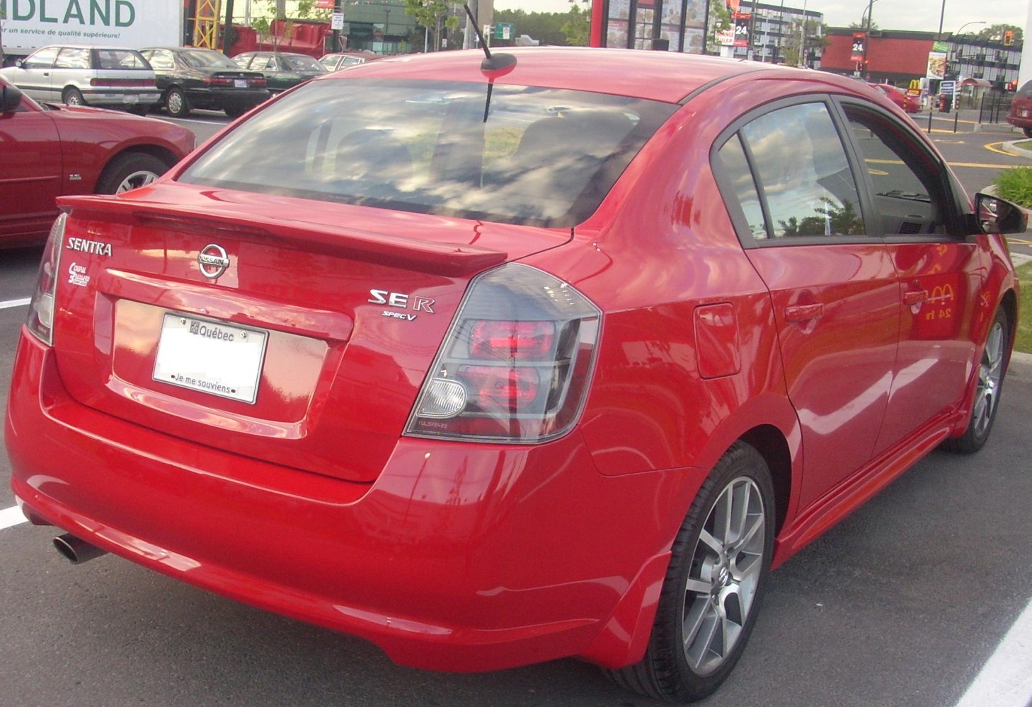 Rear and side view showing taillights, spoiler, and alloy wheels on red sedan