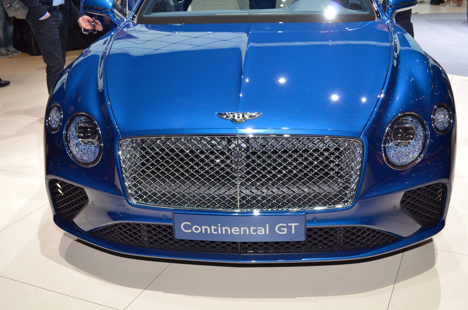 Luxury car front grille with circular headlights and chrome mesh.