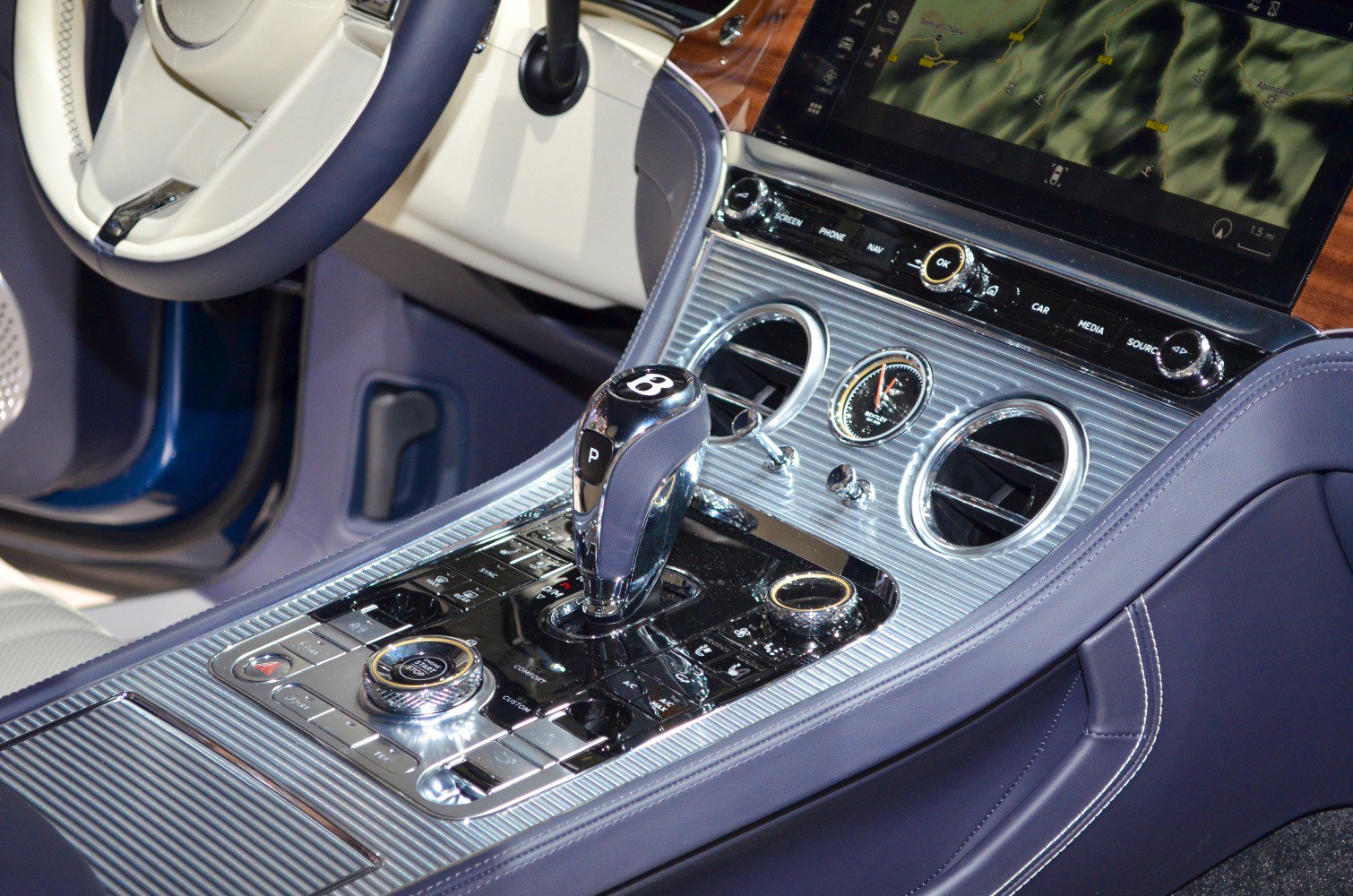 Close-up of gearshift lever and center console with analog clock and infotainment controls.