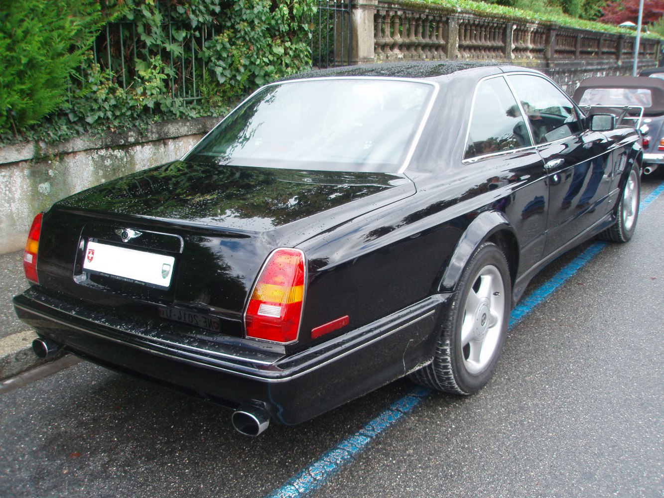Rear view of a sleek black classic luxury coupe with distinctive taillights and dual exhausts.