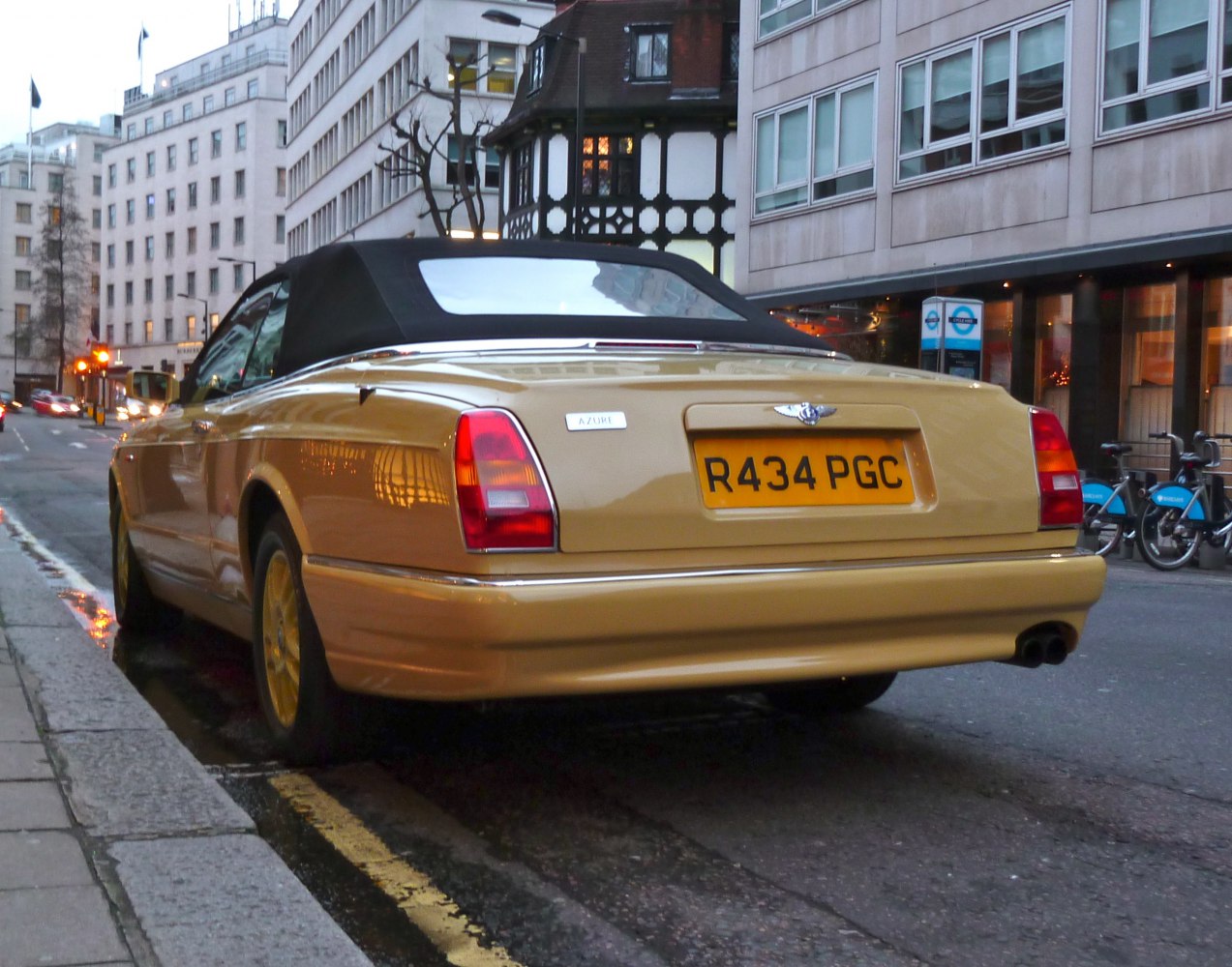 Rear view of a yellow convertible with soft top parked on a city street