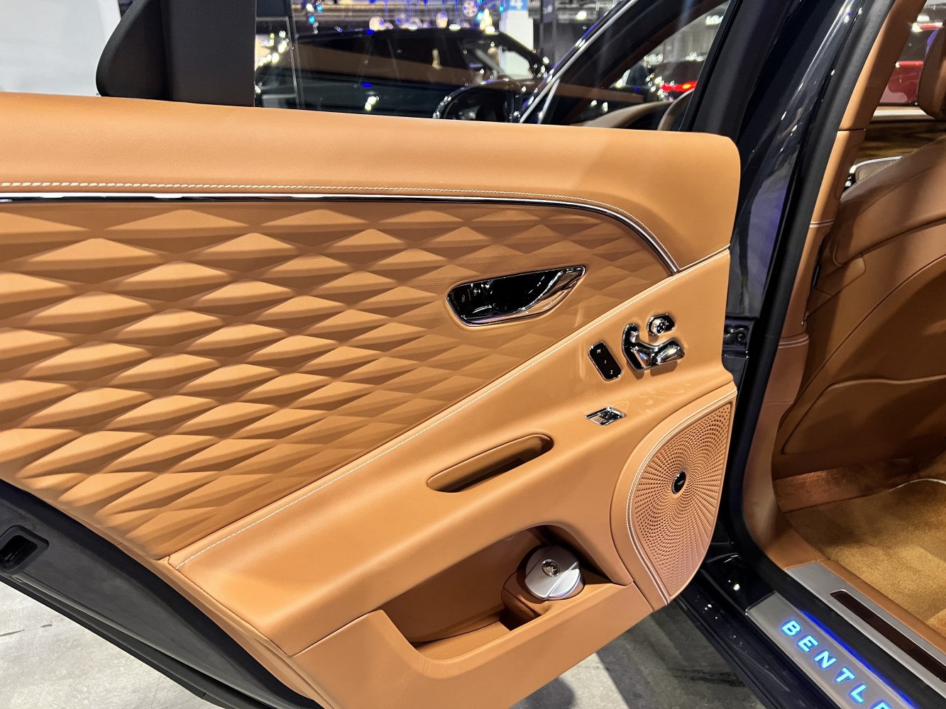 Tan leather car door panel with diamond stitching and chrome controls