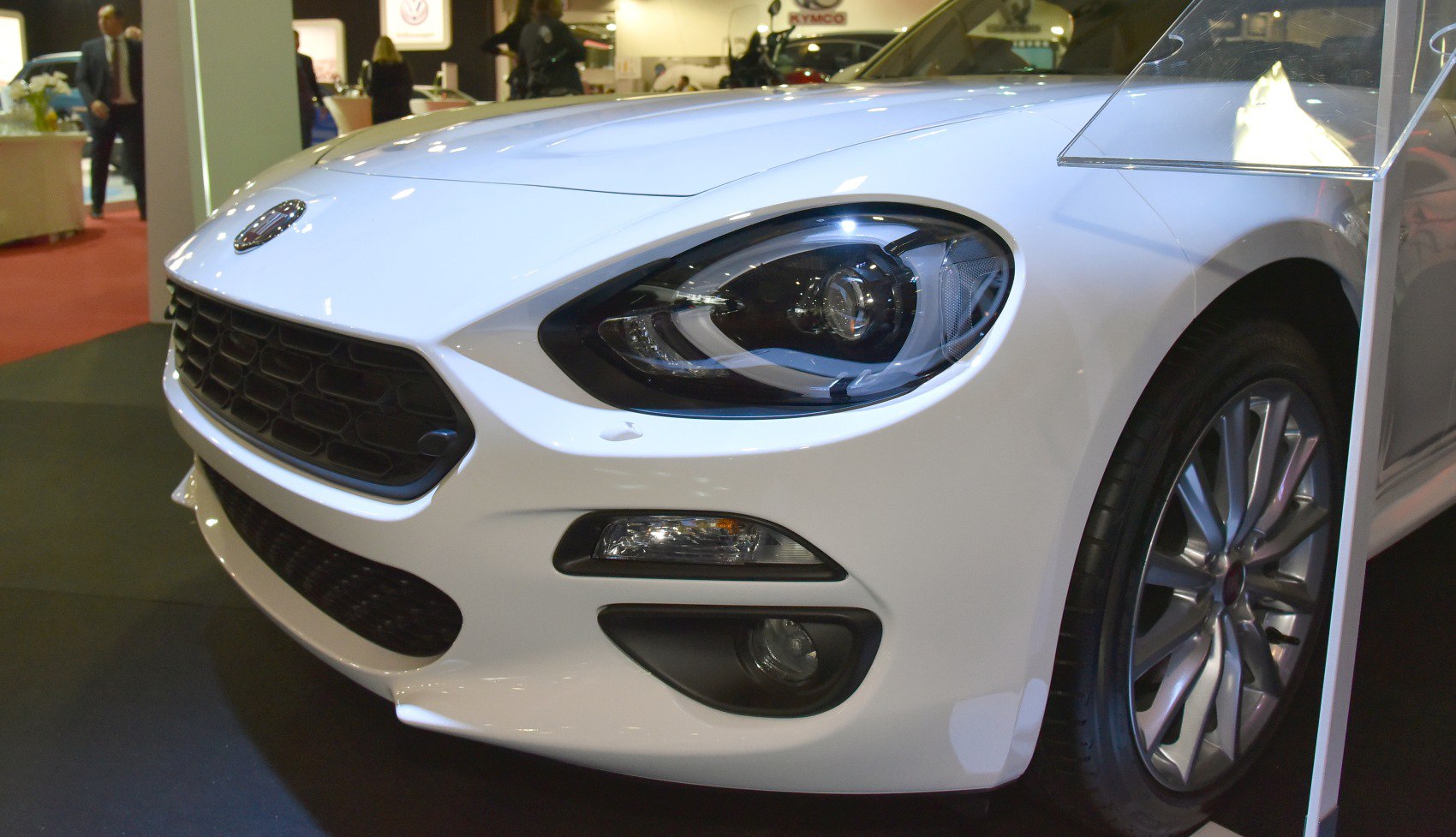 Close-up of front headlight, grille, and alloy wheel on white car