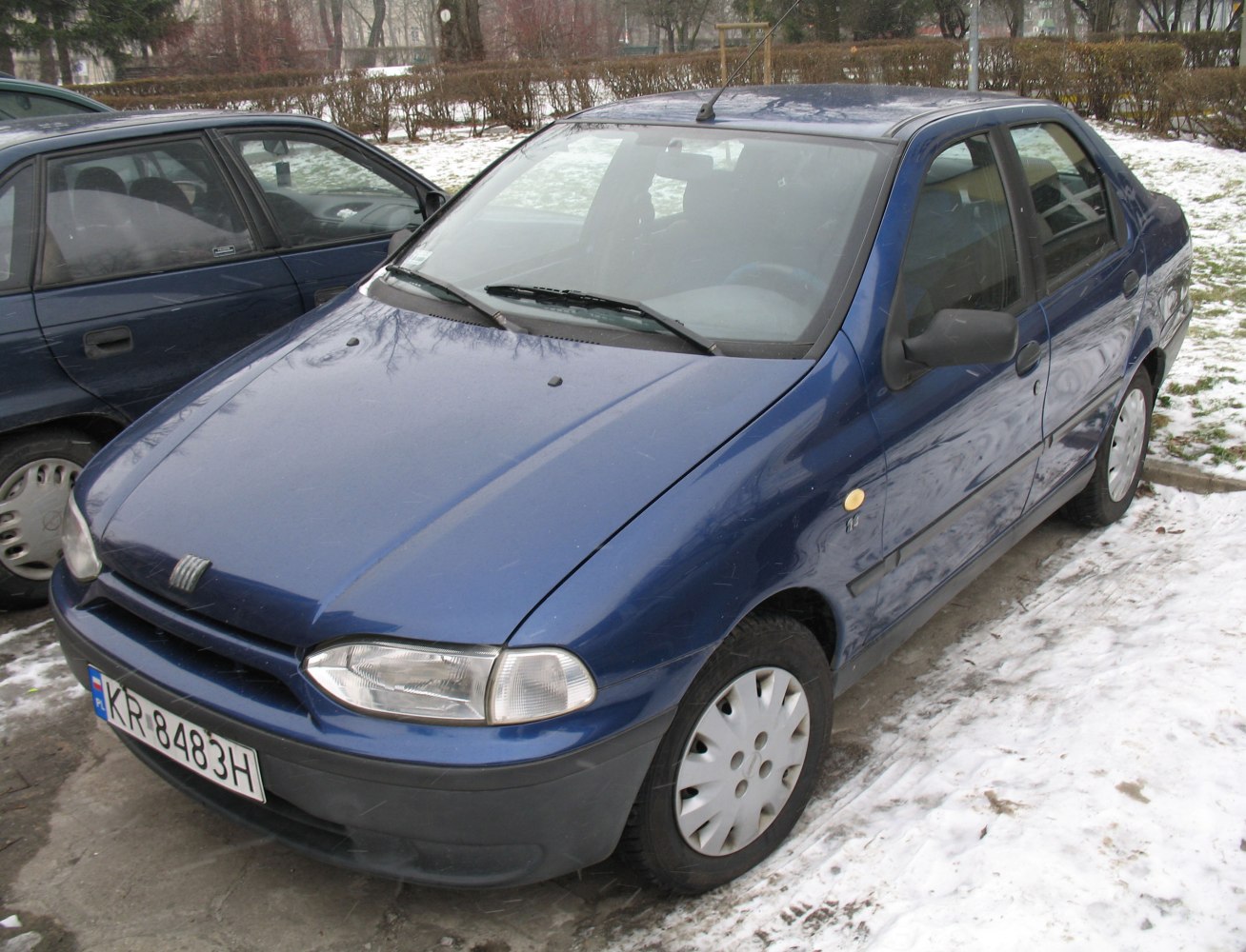 Blue sedan with rounded headlights and hubcaps parked on snowy pavement