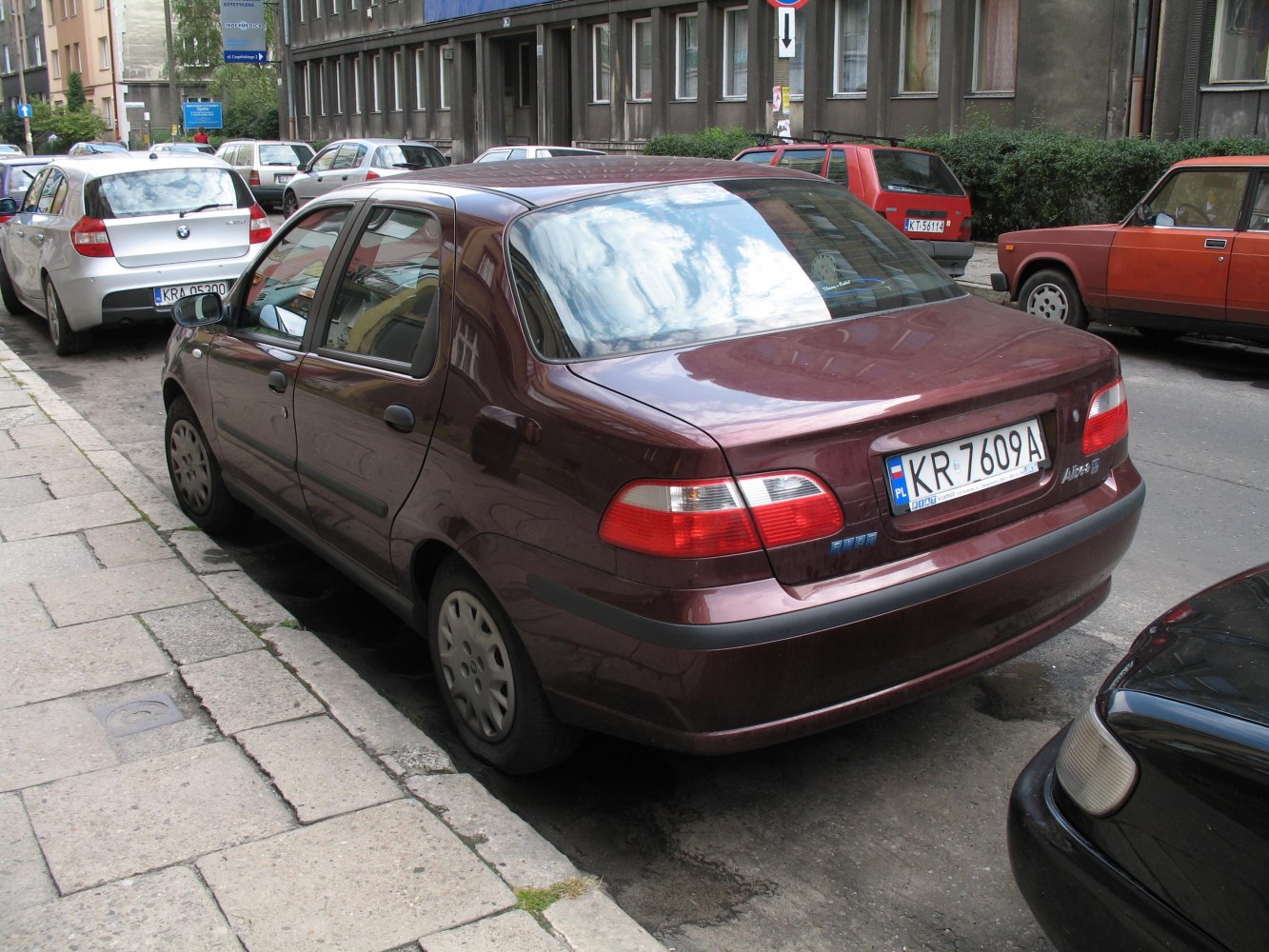 Rear-side view of a maroon four-door sedan with distinctive taillights and curved rear window.