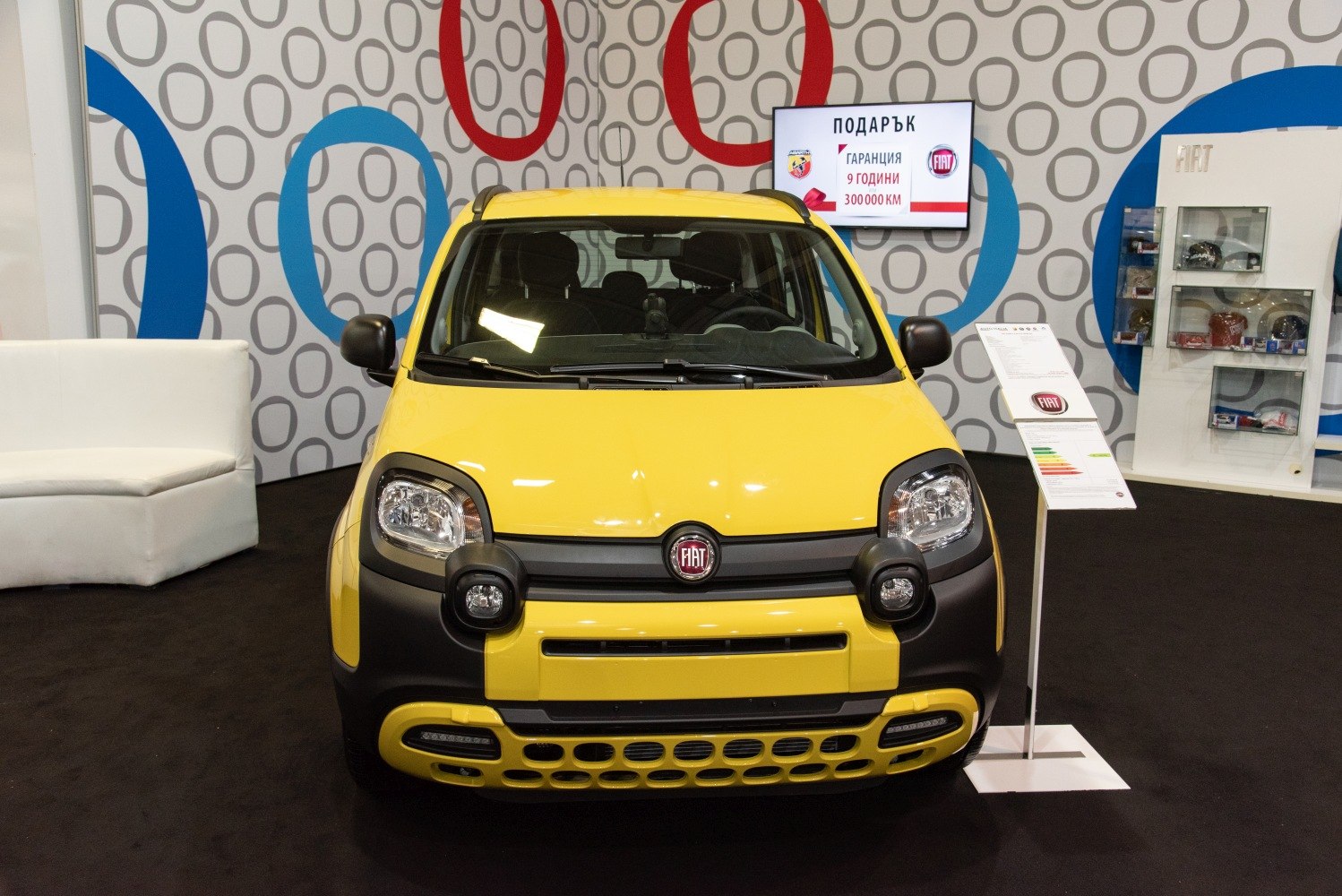 Yellow compact vehicle front view with round fog lamps and black grille.