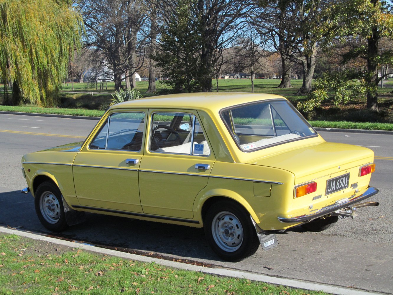 Rear-side view of vintage yellow classic four-door sedan with chrome bumper and steel wheels.