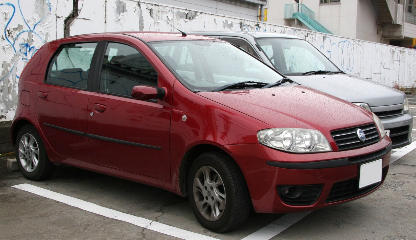 Red 5-door hatchback with front and side view, parked with wet surface.