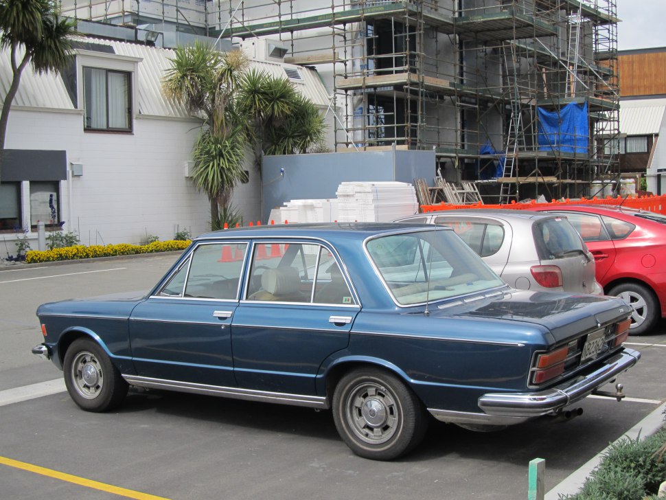 Rear three-quarter view of a classic blue four-door sedan with chrome bumpers.