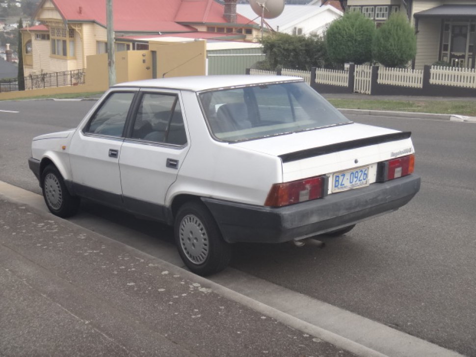 White 1980s four-door sedan rear and side profile with boxy design