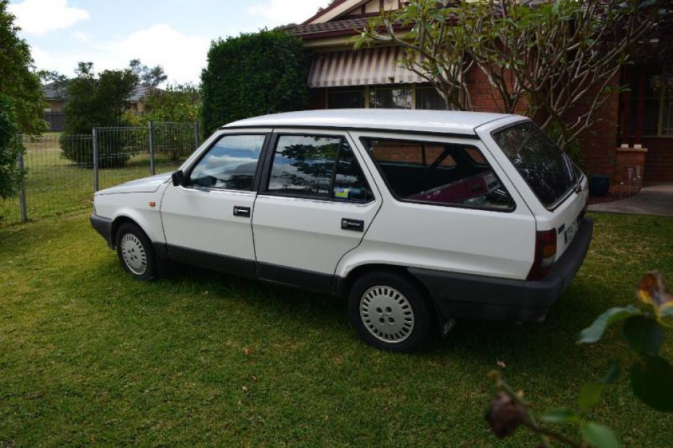Angular rear estate car with traditional hubcaps on grass in residential setting