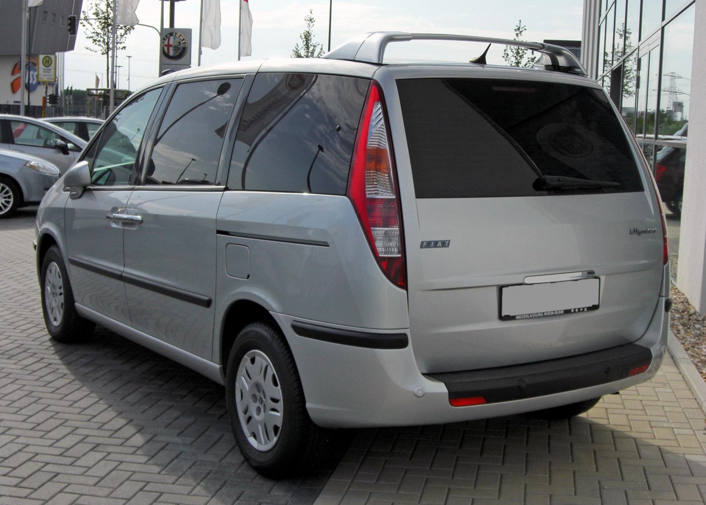 Rear and side view of a silver minivan with prominent vertical tail lights and roof rails