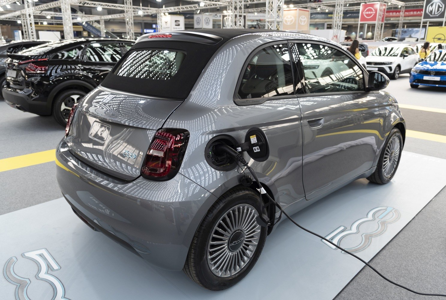 Electric compact car plugged in at charging station, showing rear and side views