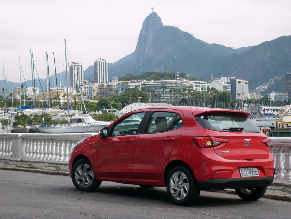 Red compact hatchback rear view by waterfront marina with sailboats.