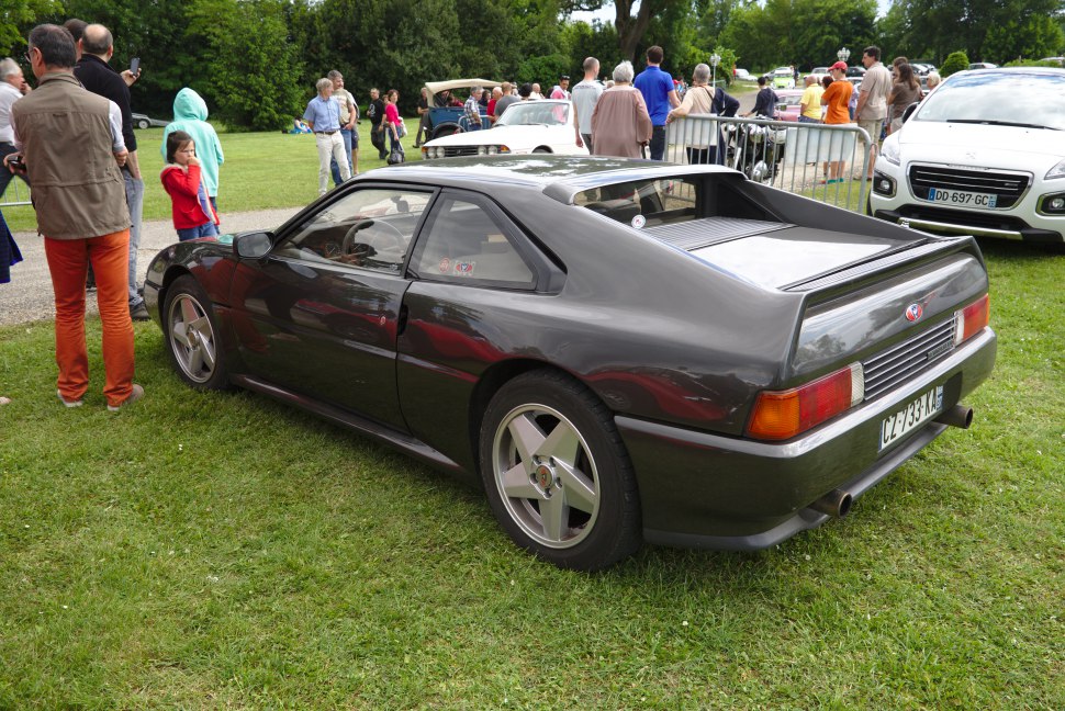 Rear quarter view of a mid-engine coupe with five-spoke wheels and angular body design