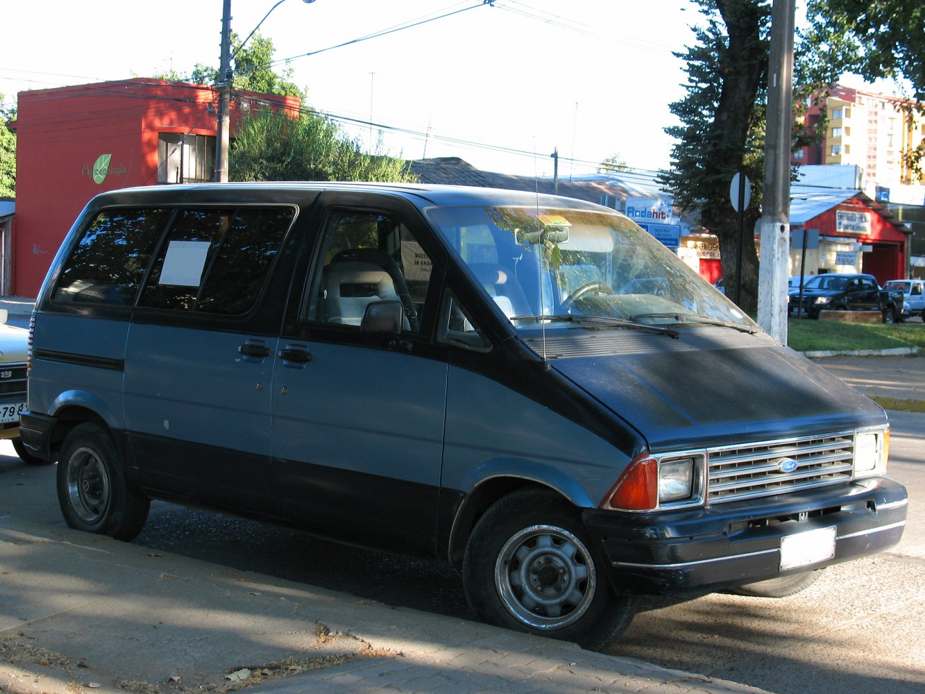 Two-tone 1980s minivan front side with boxy shape and urban background