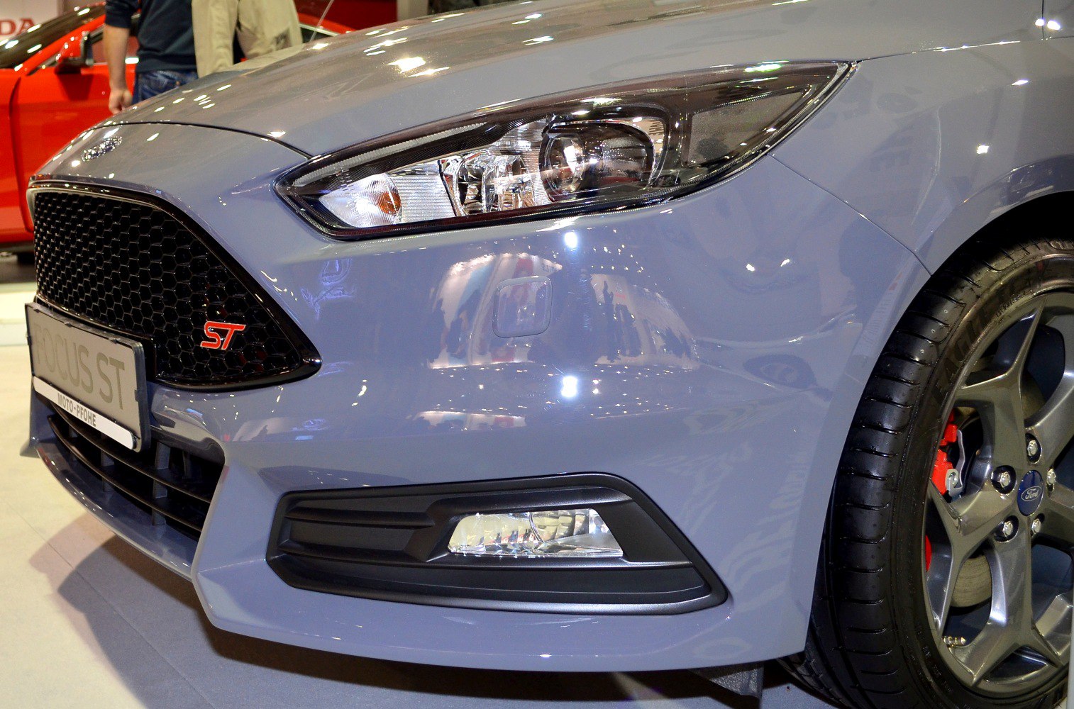Close-up of front grille, headlight, fog light, and alloy wheel with red brake calipers