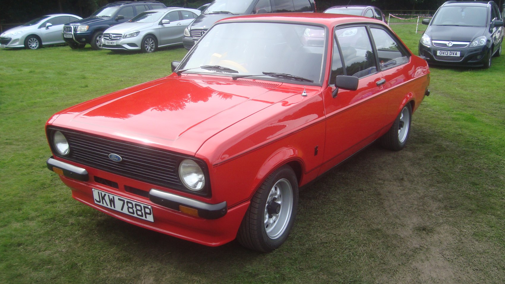 Red two-door vintage vehicle with black grille, round headlights on grass.