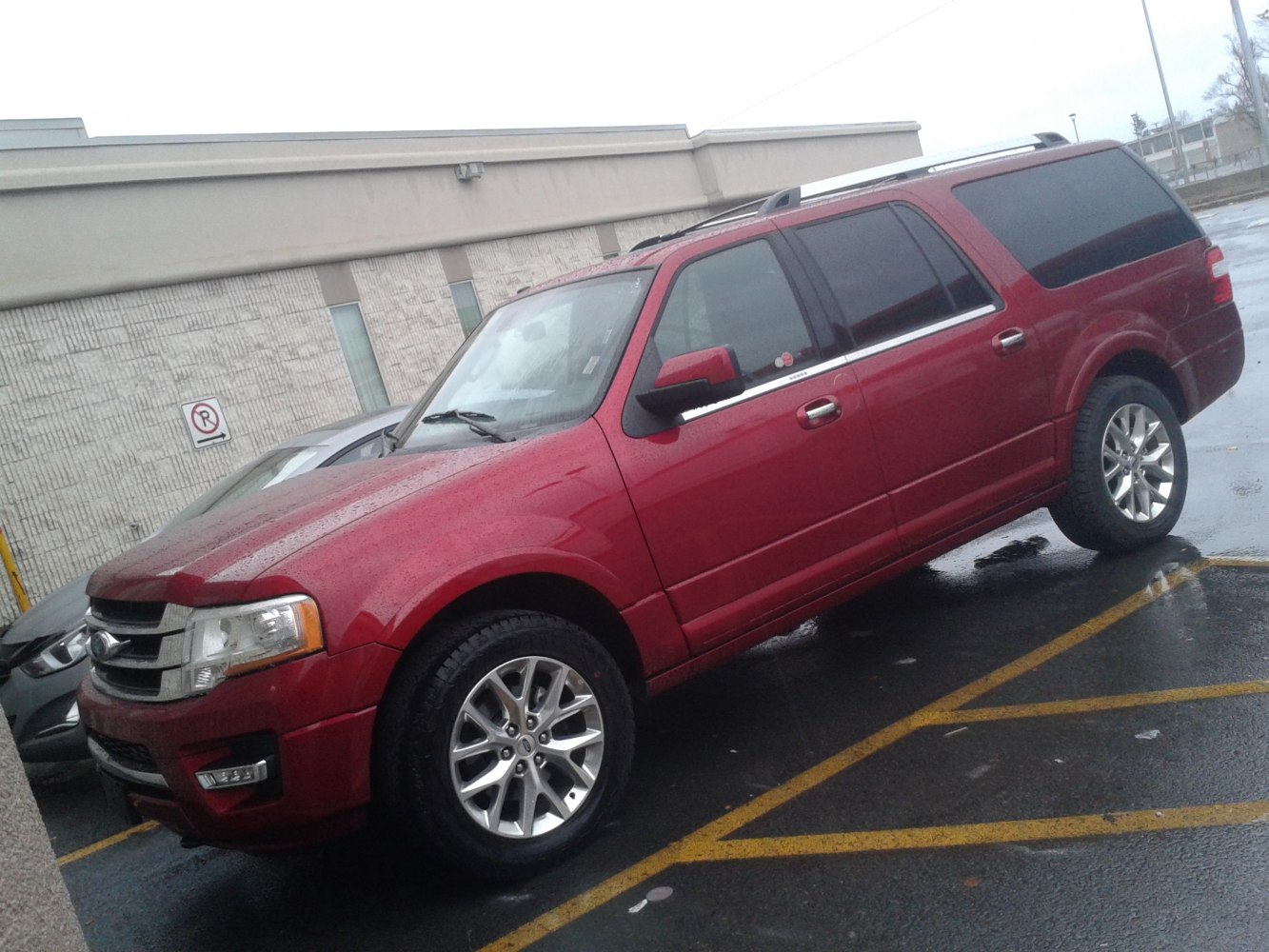 Red large SUV with chrome grille, roof rails, and alloy wheels in wet parking lot