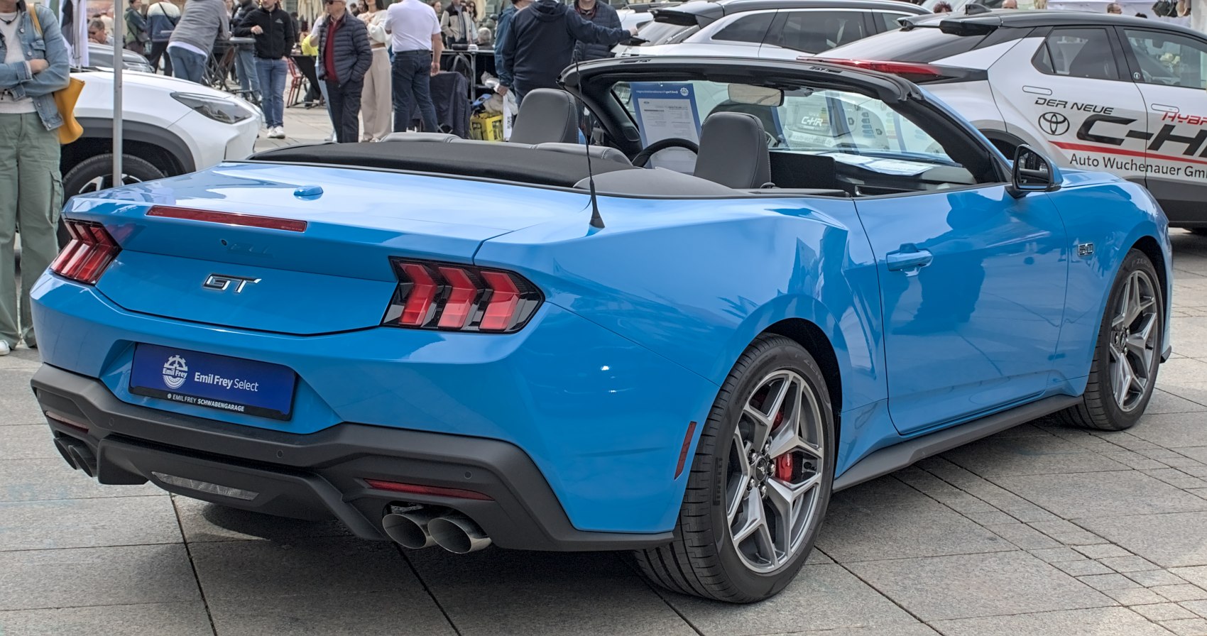 Rear view of a vibrant blue convertible with signature triple-bar taillights and dual exhaust pipes.