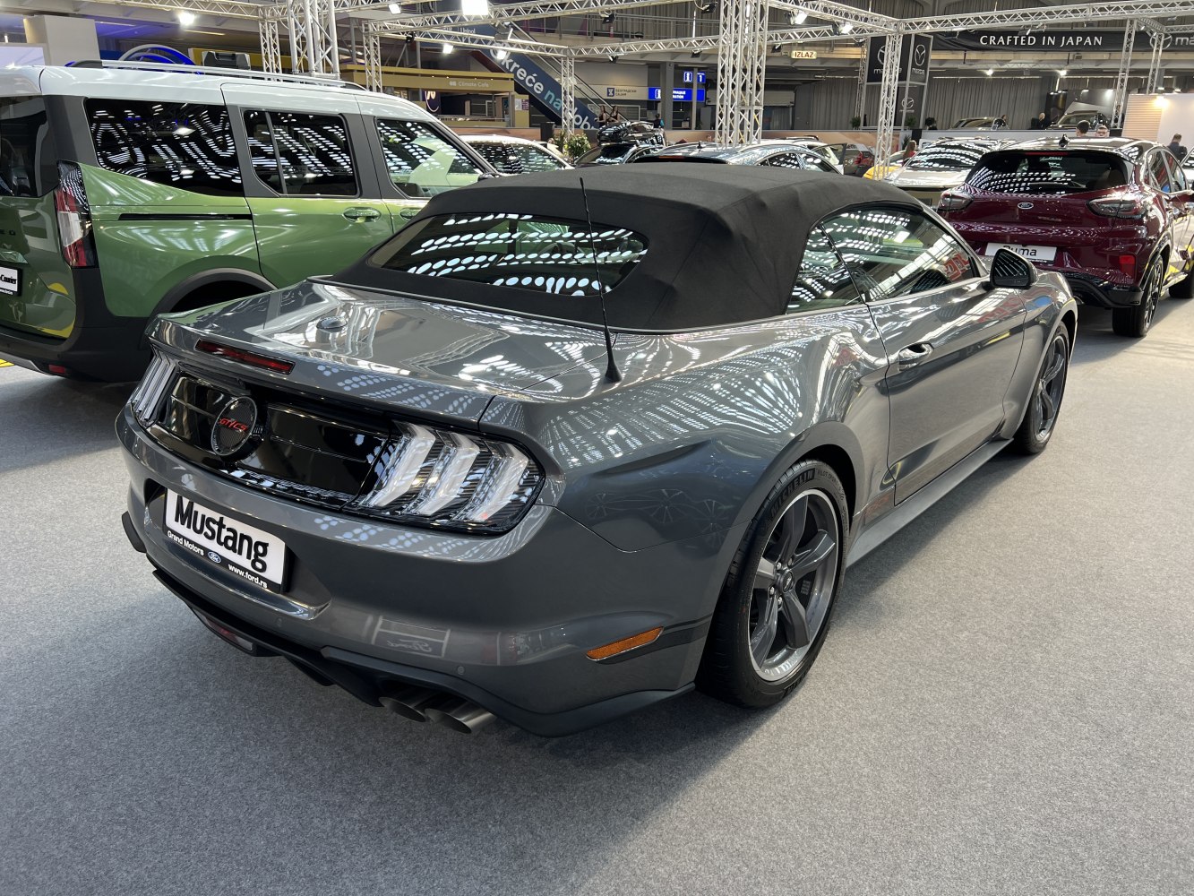 Rear side view of a grey convertible with black soft top and triple-bar taillights.