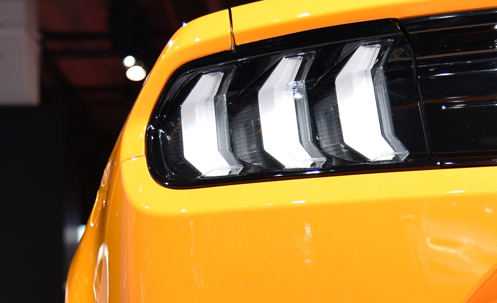 Close-up of a modern LED triple-bar rear taillight on a yellow vehicle.