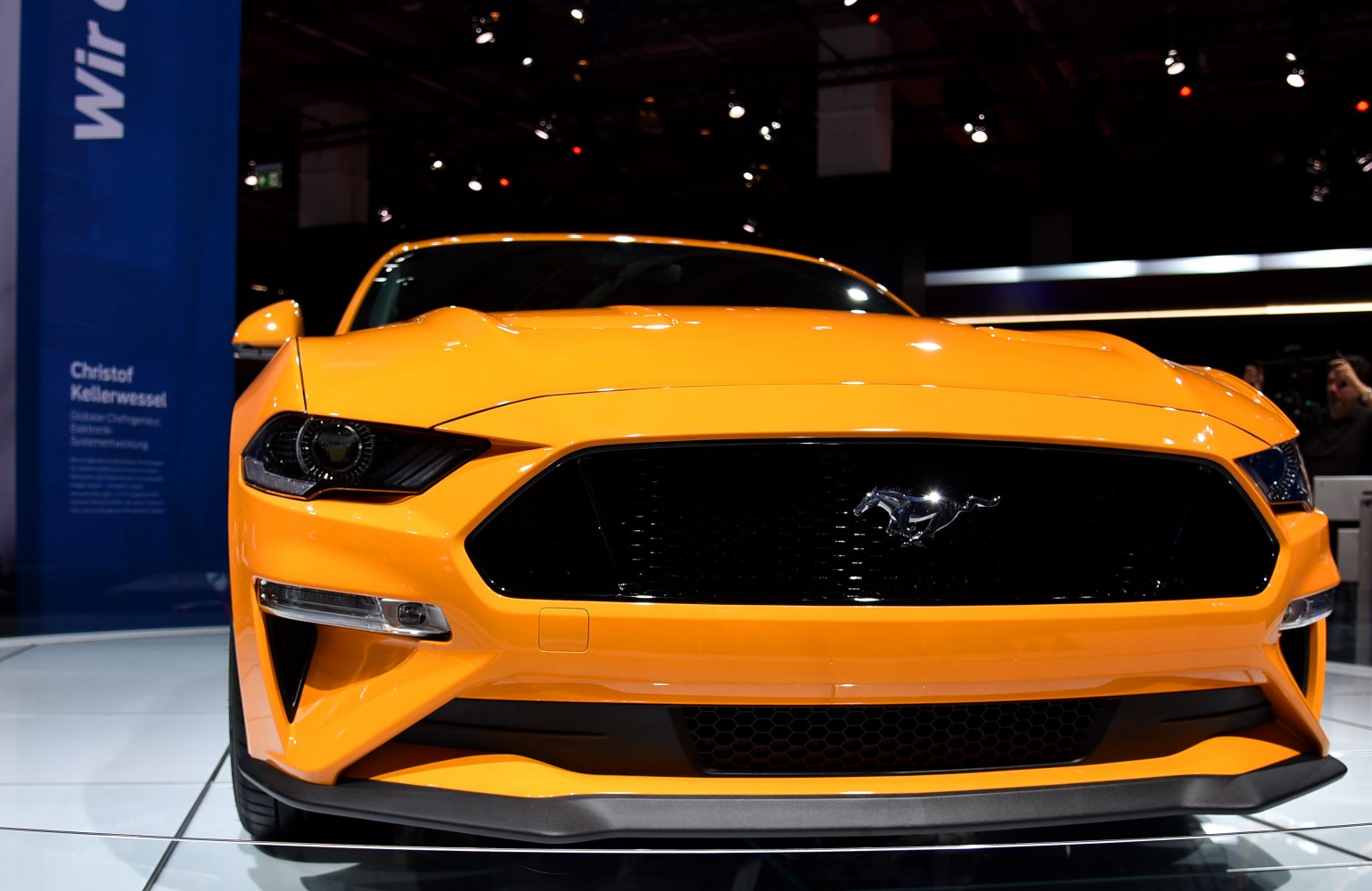 Aggressive headlights and prominent grille with emblem on bright yellow sports coupe front.