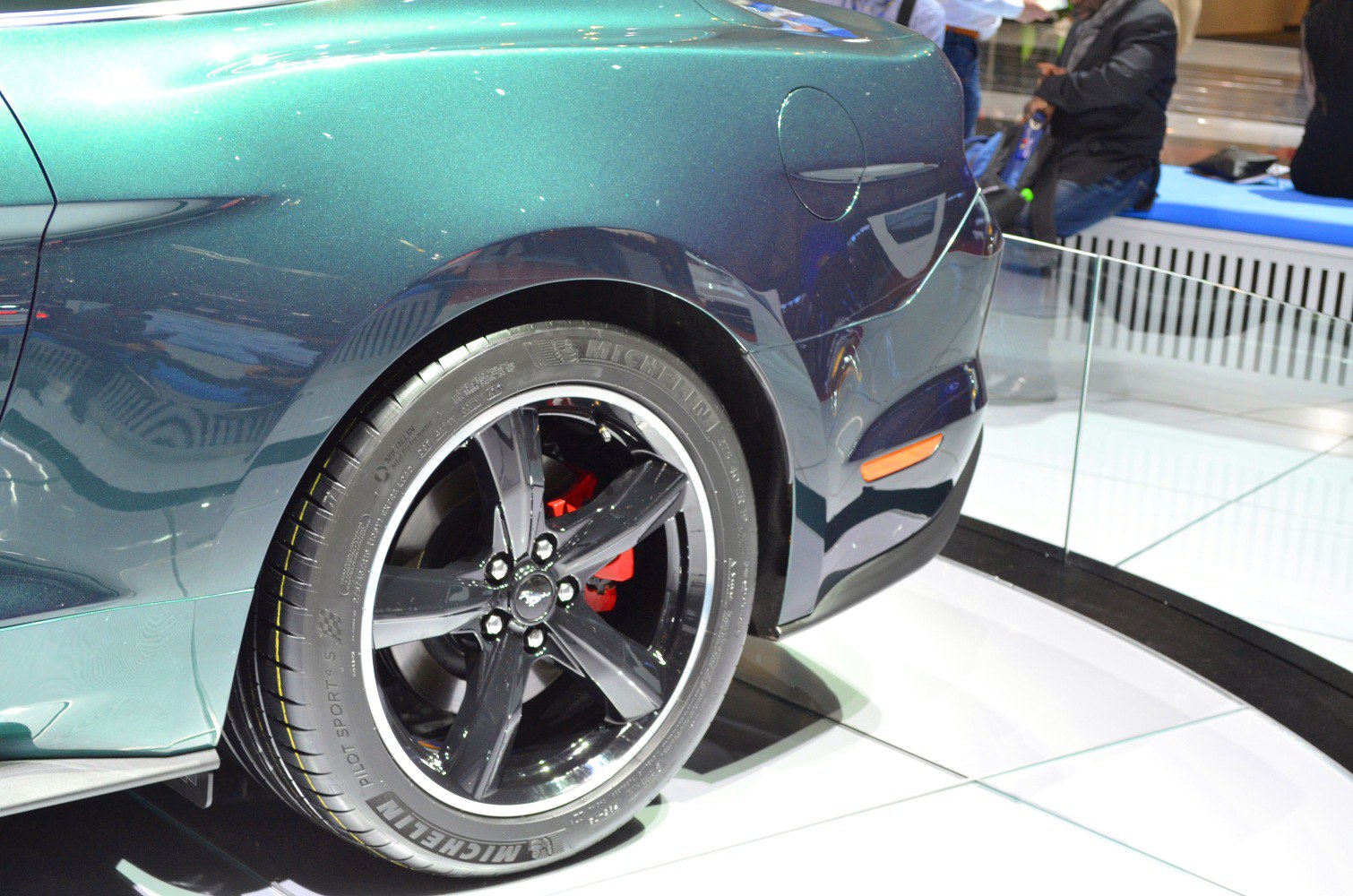 Rear black alloy wheel with red brake caliper and blue metallic fender