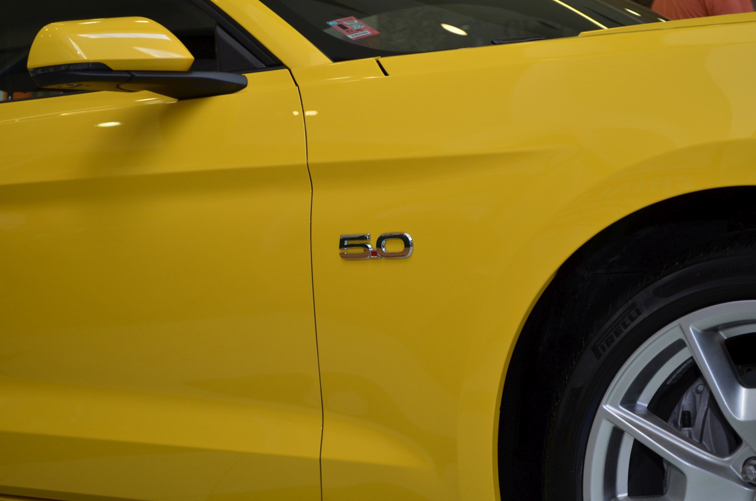 Close-up of 5.0 badge and alloy wheel on yellow car side panel