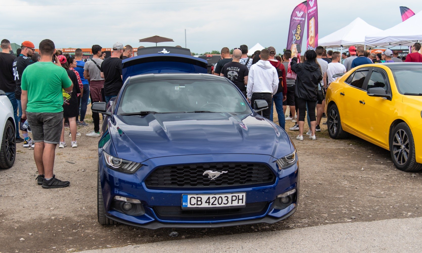 Front view of blue muscle car with honeycomb grille and open trunk