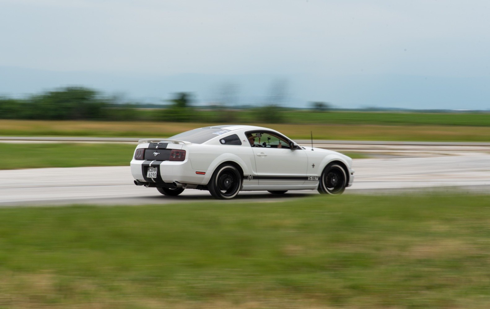 White sporty coupe with black racing stripes and spoiler in motion on track