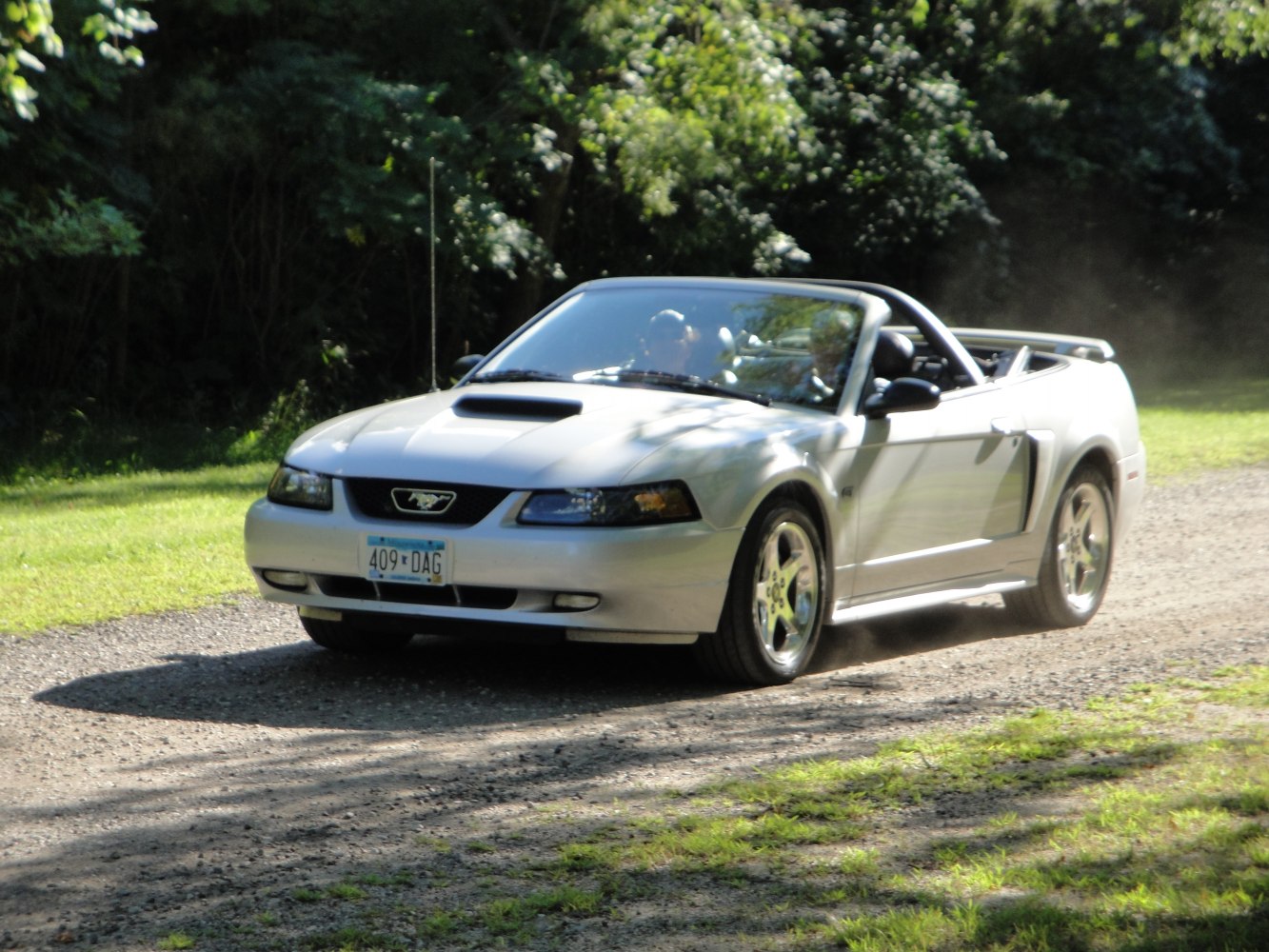 Silver convertible with hood scoop and rear spoiler on gravel path
