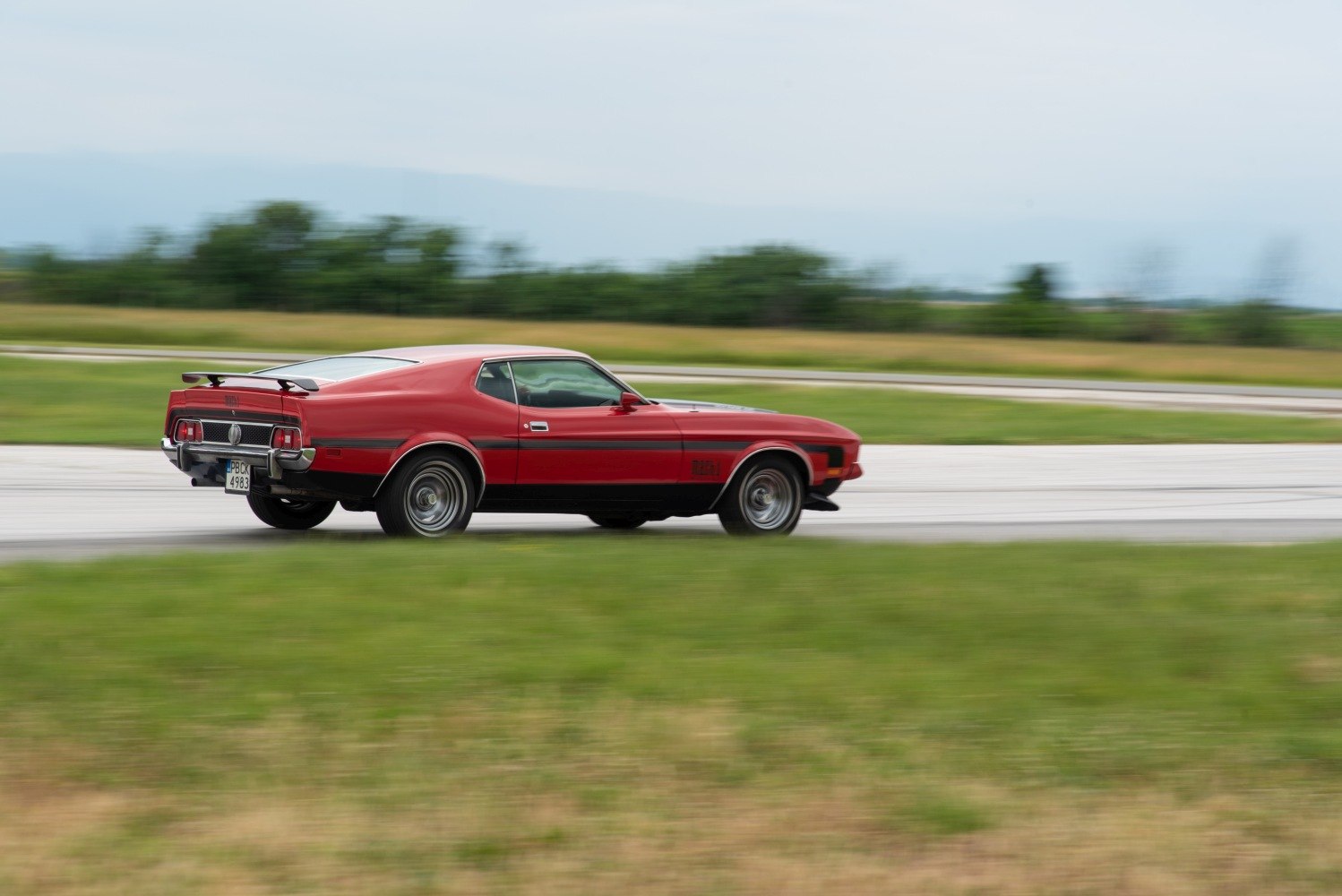 Red classic muscle car rear side view with spoiler in motion